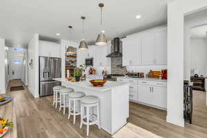 Kitchen featuring tasteful backsplash, appliances with stainless steel finishes, a kitchen breakfast bar, white cabinets, and light wood-type flooring