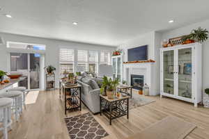 Living area with light wood finished floors, a textured ceiling, recessed lighting, and a glass covered fireplace