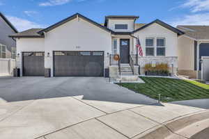 View of front of property with a front lawn, a garage, driveway, and stone siding
