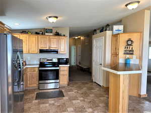 Kitchen with appliances with stainless steel finishes, lofted ceiling, stone finish floors, light countertops, and under cabinet range hood