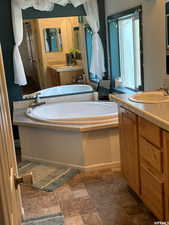 Bathroom featuring two vanities, a bath, and dark stone finish flooring