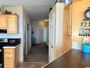 Kitchen with stainless steel electric range oven, light brown cabinetry, black microwave, exhaust hood, and dark colored carpet