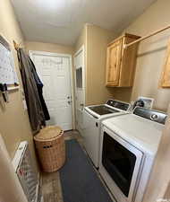 Washroom featuring cabinet space, a textured ceiling, washer and clothes dryer, and dark stone finish flooring