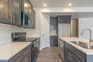 Kitchen with appliances with stainless steel finishes, dark wood finished floors, light stone counters, recessed lighting, and dark brown cabinets