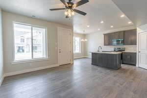 Kitchen with a textured ceiling, an island with sink, plenty of natural light, dark brown cabinets, and stainless steel appliances