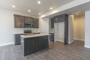 Kitchen featuring dark brown cabinets, recessed lighting, appliances with stainless steel finishes, dark wood-style floors, and an island with sink