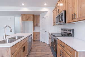 Kitchen with appliances with stainless steel finishes, dark wood-type flooring, a kitchen island with sink, recessed lighting, and light stone counters