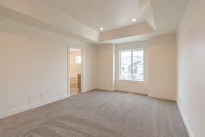 Unfurnished bedroom with light carpet, a tray ceiling, and recessed lighting