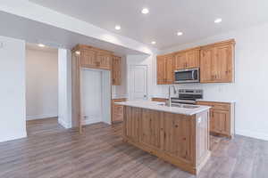 Kitchen with recessed lighting, appliances with stainless steel finishes, dark wood-style floors, a kitchen island with sink, and light stone countertops