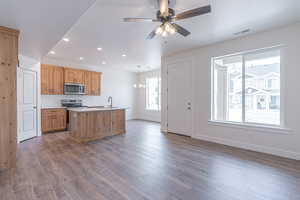 Kitchen featuring recessed lighting, appliances with stainless steel finishes, light countertops, dark wood-type flooring, and an island with sink