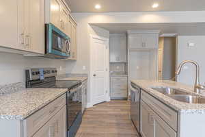 Kitchen with stainless steel appliances, light wood-style flooring, light stone countertops, recessed lighting, and an island with sink