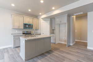 Kitchen with light stone counters, stainless steel appliances, recessed lighting, a kitchen island with sink, and gray cabinetry