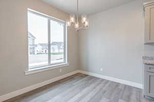 Unfurnished dining area with light wood-type flooring, a chandelier, and a residential view
