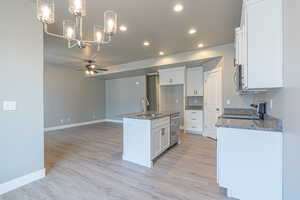 Kitchen featuring a ceiling fan, hanging light fixtures, a center island with sink, recessed lighting, and dark stone counters
