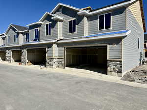 Craftsman-style home featuring stone siding, a garage, and driveway