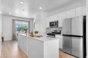 Kitchen featuring stainless steel appliances, white cabinetry, a center island with sink, light wood-style floors, and recessed lighting