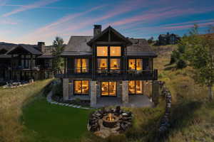Back of property at dusk with a fire pit, a patio, a chimney, and a lawn