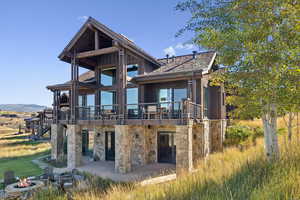 Back of house with a patio area, an outdoor fire pit, stone siding, board and batten siding, and a wooden deck