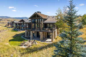 Back of house featuring stone siding, an outdoor fire pit, a patio, a yard, and a deck with mountain view