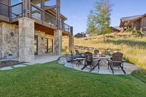 View of grassy yard with a patio, a fire pit, and a balcony