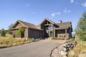 View of front of home with a chimney, driveway, an attached garage, and stone siding