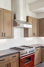 Kitchen featuring wall chimney exhaust hood, range with gas cooktop, decorative backsplash, and brown cabinets