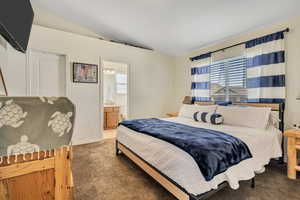 Carpeted bedroom featuring lofted ceiling and ensuite bath