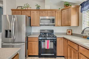 Kitchen with stainless steel appliances, vaulted ceiling, light stone countertops, and brown cabinetry