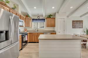Kitchen featuring appliances with stainless steel finishes, beamed ceiling, a center island, recessed lighting, and light countertops