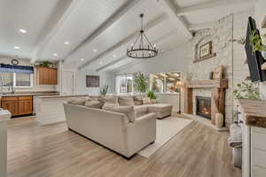 Living area featuring light wood-style floors, a stone fireplace, healthy amount of natural light, a chandelier, and recessed lighting