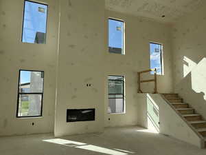 Unfurnished living room with a towering ceiling, stairway, and a glass covered fireplace