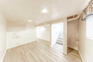 Finished below grade area featuring a textured ceiling, light wood finished floors, and stairs