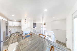 Kitchen with freestanding refrigerator, light wood-style floors, a kitchen island, white cabinetry, and decorative light fixtures