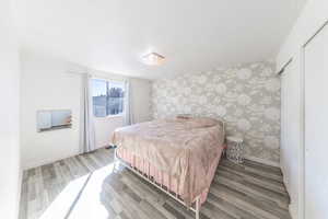 Bedroom with wallpapered walls, light wood finished floors, and an accent wall