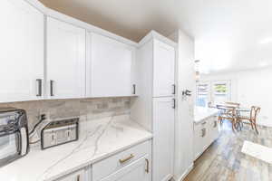Kitchen with white cabinetry, decorative backsplash, and light stone counters