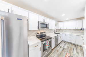 Kitchen with appliances with stainless steel finishes, white cabinetry, backsplash, and recessed lighting