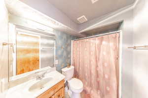 Full bathroom featuring vanity, wallpapered walls, a shower with shower curtain, a textured ceiling, and vaulted ceiling
