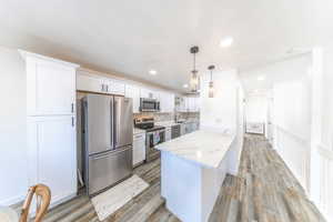 Kitchen with appliances with stainless steel finishes, decorative light fixtures, white cabinets, a peninsula, and light stone counters