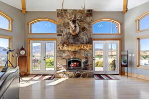Living room with a stone fireplace, wood finished floors, a towering ceiling, and french doors