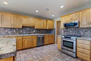 Main floor Kitchen featuring stainless steel appliances, tasteful backsplash, light stone countertops, recessed lighting, and a textured ceiling