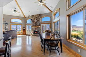 Dining area with a fireplace, high vaulted ceiling, light wood-style floors, ceiling fan, and french doors