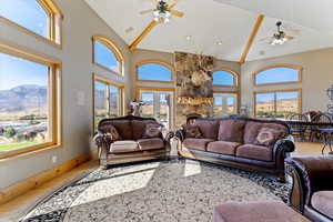 Living room with wood finished floors, a ceiling fan, high vaulted ceiling, a fireplace, and french doors