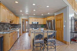 Main floor Kitchen featuring a breakfast bar area, stainless steel appliances, a textured ceiling, recessed lighting, and a kitchen island