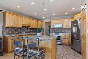 Main floor Kitchen with appliances with stainless steel finishes, a breakfast bar area, recessed lighting, a center island, and tasteful backsplash