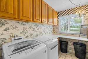 Washroom featuring wallpapered walls, light tile patterned floors, a chandelier, washer and dryer, and cabinet space