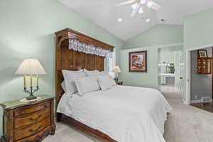 Bedroom with carpet flooring, vaulted ceiling, ceiling fan, and connected bathroom