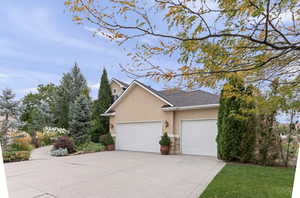 View of side of property with stucco siding, driveway, stone siding, a garage, and a shingled roof