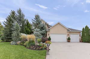 View of front of home with stucco siding, a garage, concrete driveway, a front lawn, and stone siding