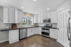 Kitchen featuring white cabinets, appliances with stainless steel finishes, dark wood-type flooring, tasteful backsplash, and recessed lighting