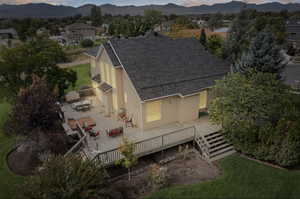 Back of property at dusk with a shingled roof, stucco siding, a deck with mountain view, and outdoor dining space